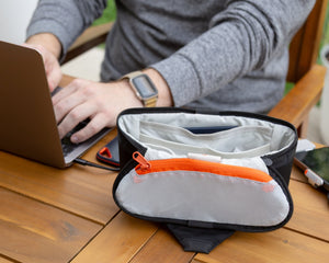 Person using a laptop with a small bag on a wooden table outdoors
